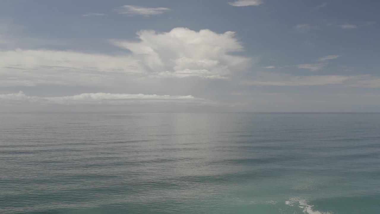 Open ocean and layered clouds under a muted blue sky.