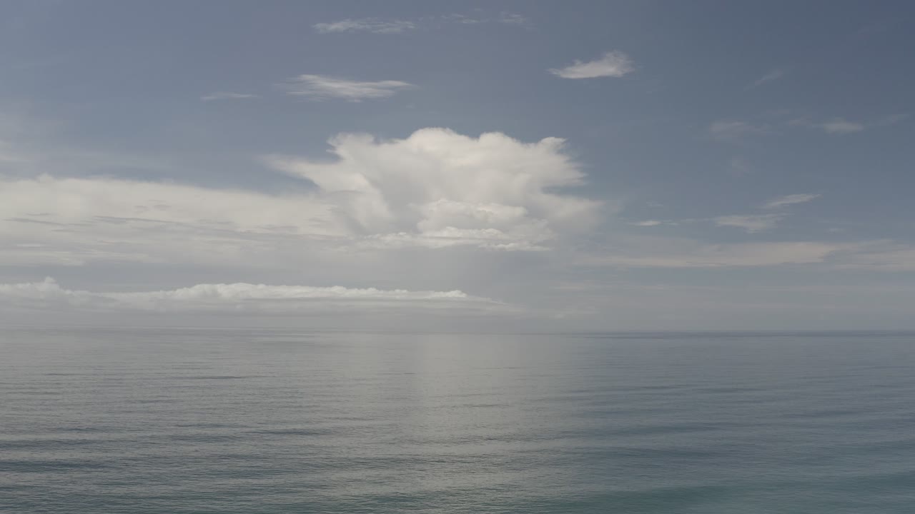 Wide Los Cabos ocean view at the start of the clip, with a pale cloud bank mirrored on the water and no visible people.