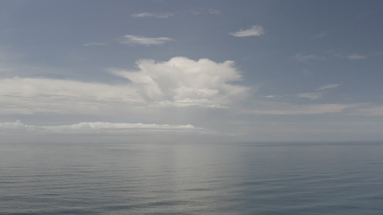 Opening view of the Los Cabos ocean horizon under pale blue sky, with broad white clouds and no visible people.