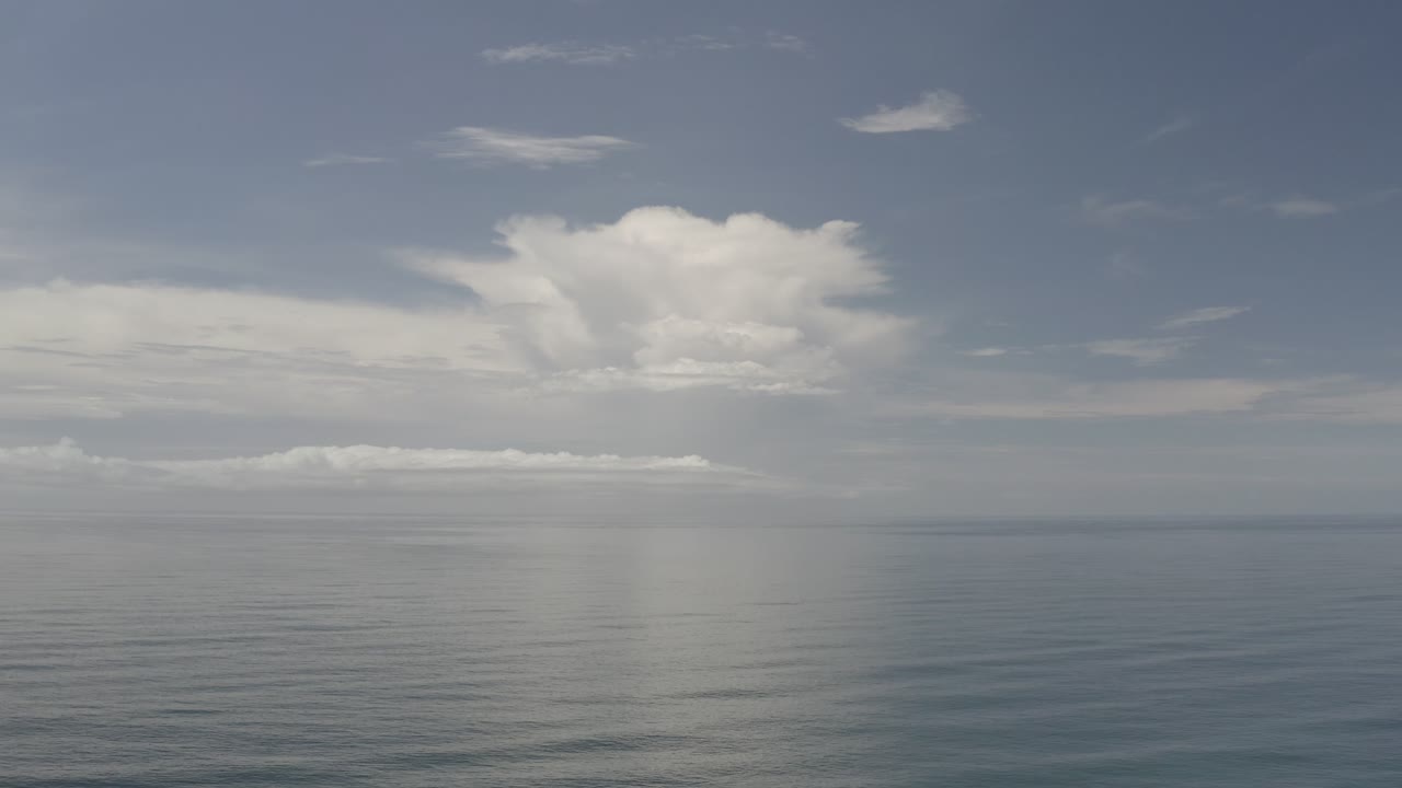 Wide Los Cabos ocean view with a low cloud bank near the horizon, a larger cloud mass above, and no visible people.