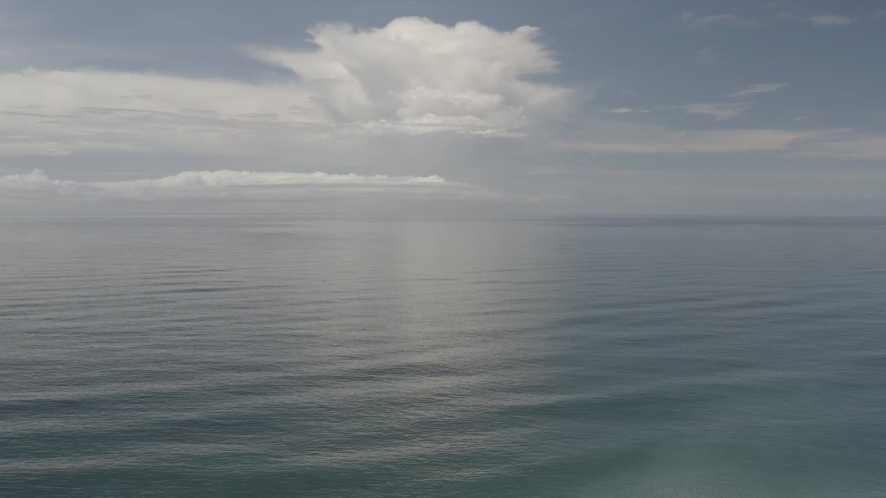 Wide Los Cabos ocean view with calm blue-green water, a level horizon, layered gray-white clouds, and no visible people.