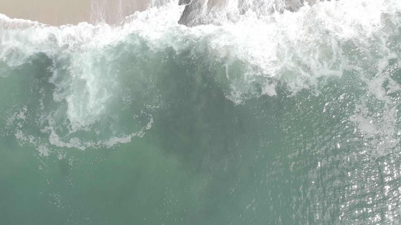 A Los Cabos wave break spreads farther across the gray-green ocean surface, with bright foam bands and no visible people.