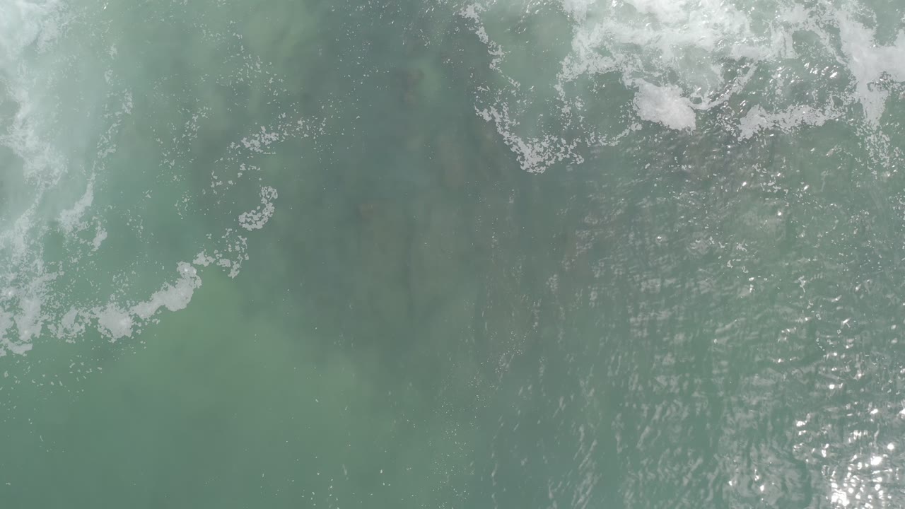 Overhead Los Cabos ocean water shows a broader patch of foam near the top, green-gray ripples below, and no visible people.