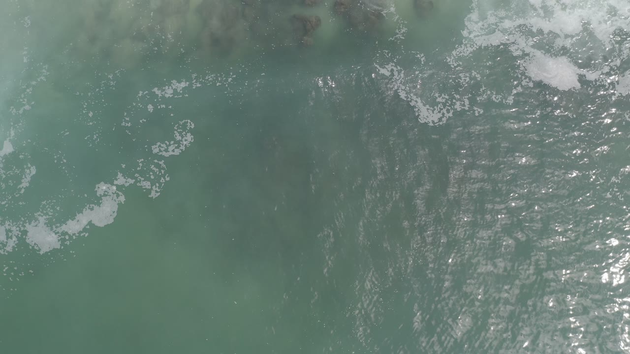 Green coastal water seen from above with foam drifting across the frame.