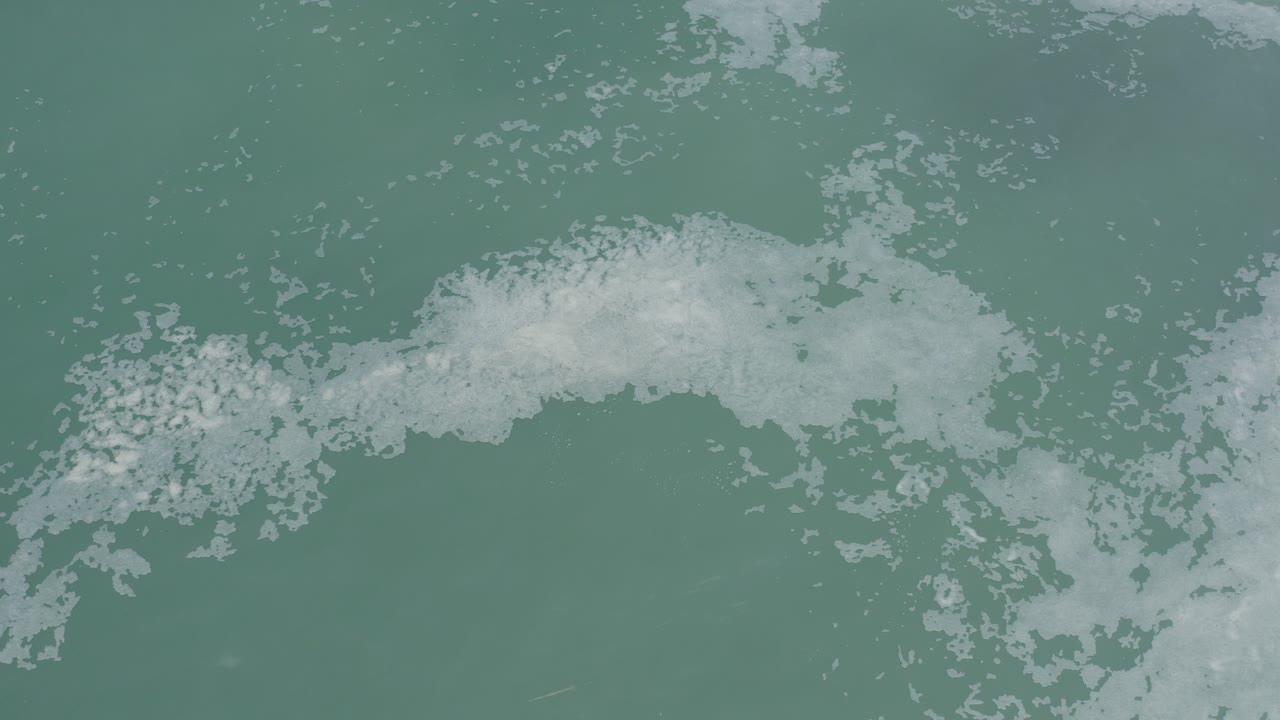 White sea foam crossing blue-green ocean water from above.