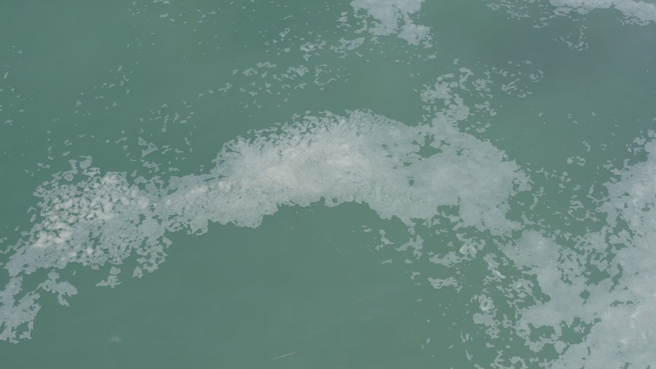 White foam gathers in a broad band across muted turquoise water in Los Cabos, Mexico, with no visible people.