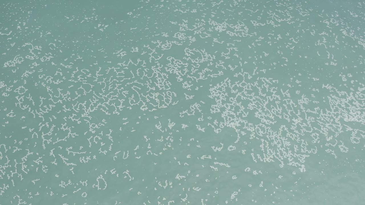 A later overhead frame shows Los Cabos water filled with tighter white ripple patterns and faint cloudy areas below the surface, with no visible people.