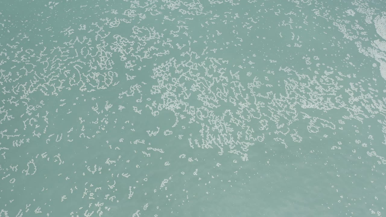 Overhead water texture with pale foam scattered over blue-green water.