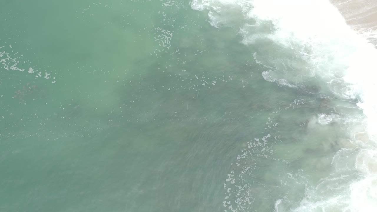 Blue-green shallow water with surf foam clustered at the upper right.