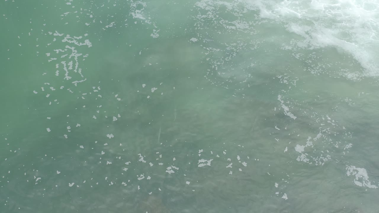 Top-down Los Cabos seawater shows white foam streaks spread across muted green water, with no visible people or shoreline.