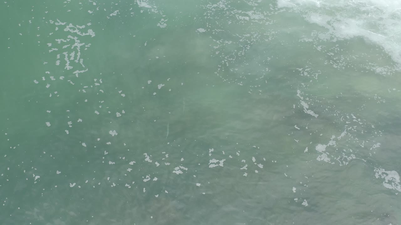 Aerial ocean detail with foam clustered along the upper right
