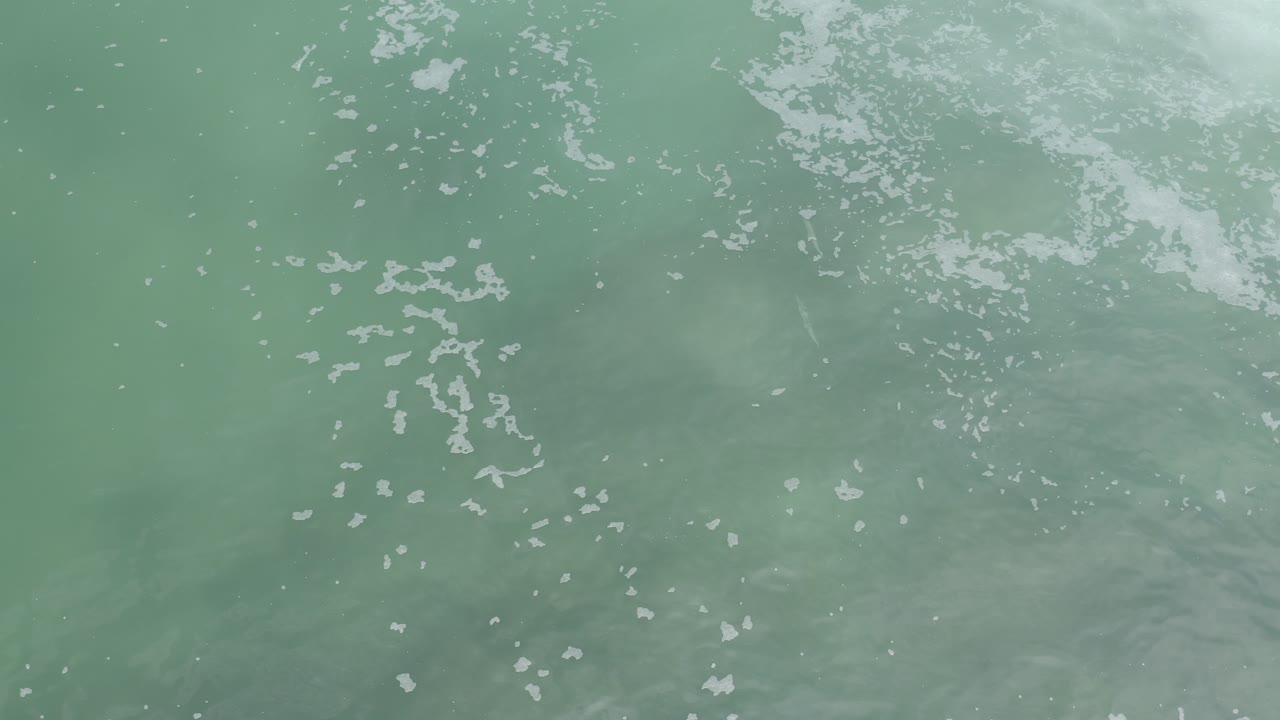 Overhead view of green-blue water with scattered white foam.