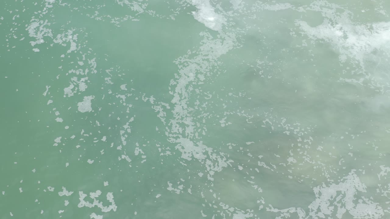Los Cabos sea water fills the frame with a faint diagonal foam streak near the upper area and scattered bubbles below, with no visible people.