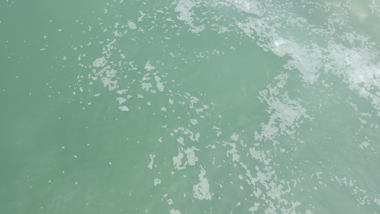 Pale green surf water with broken white foam patterns.