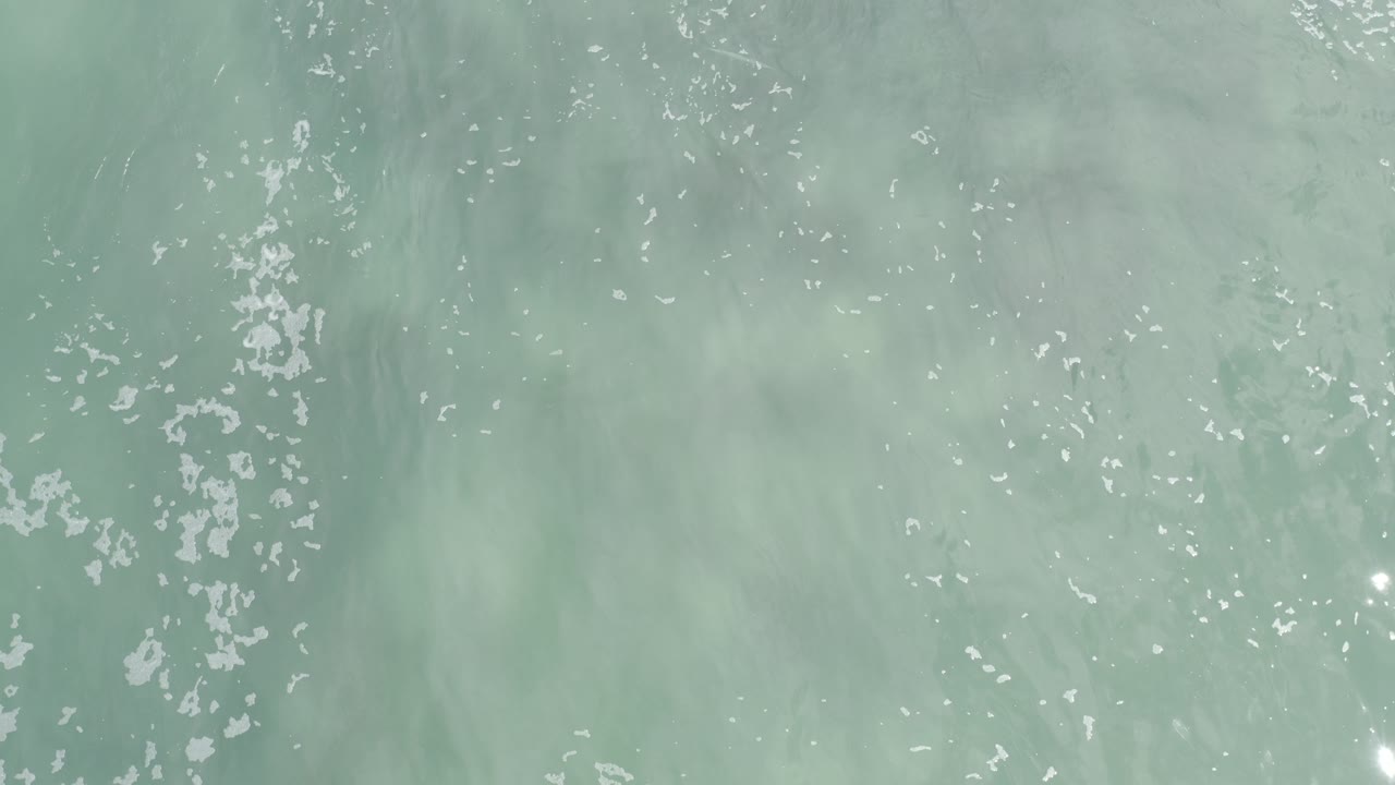 Top-down pale turquoise ocean water with scattered white foam.