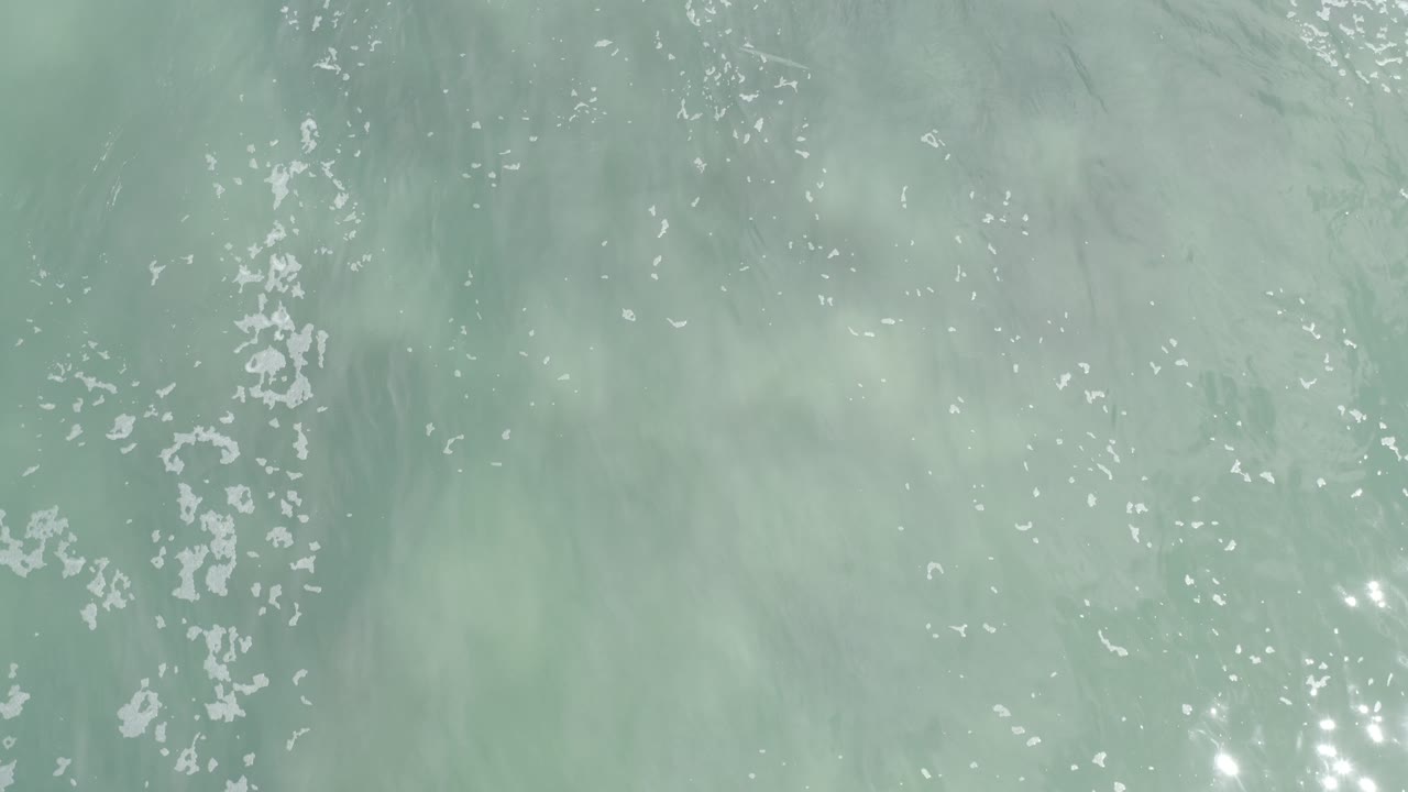 Aerial water texture with pale surf and small bright reflections.