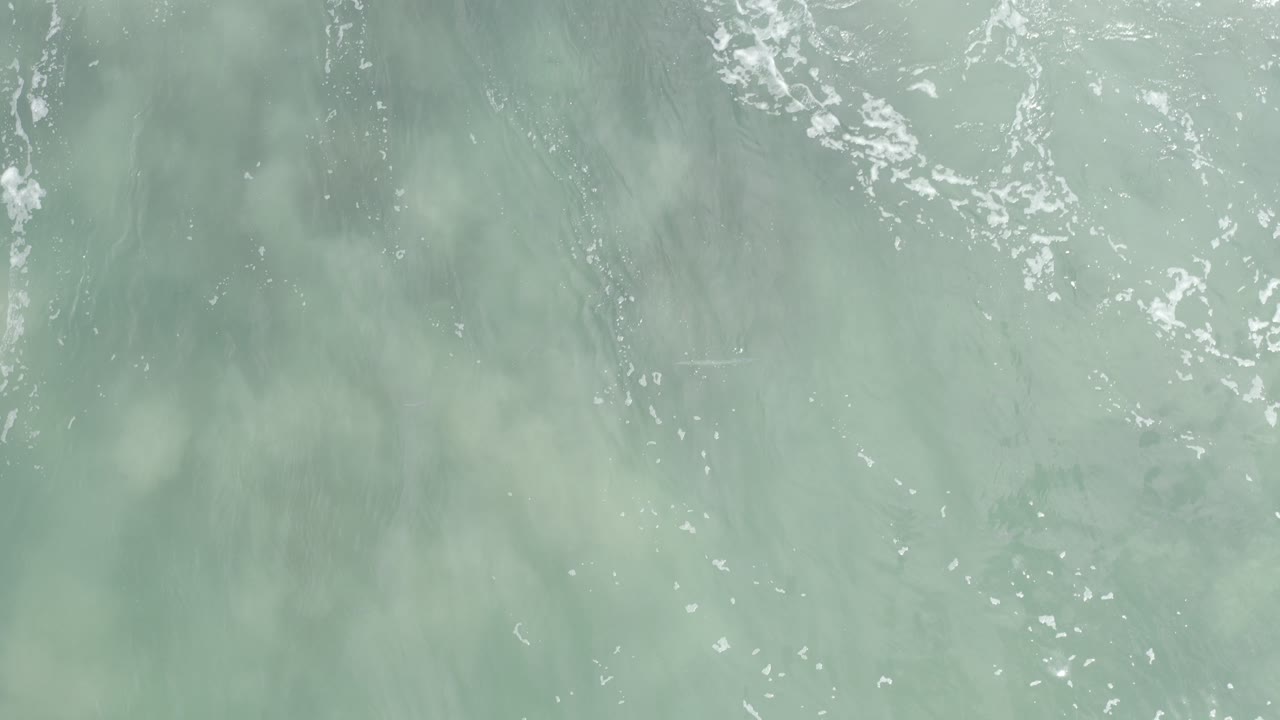Pale gray-green ocean water with white foam streaks.