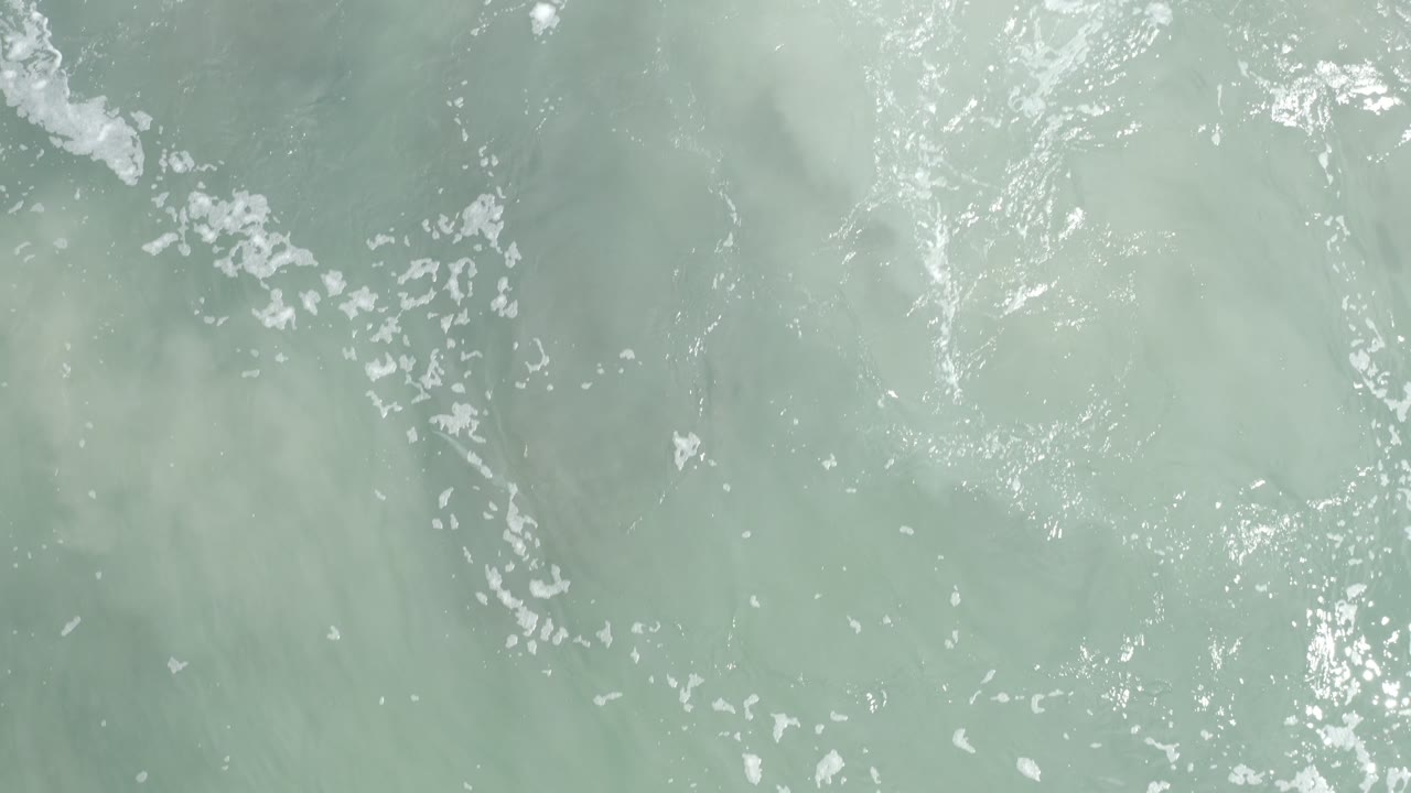 Turquoise water with foam clusters and rippled sunlight