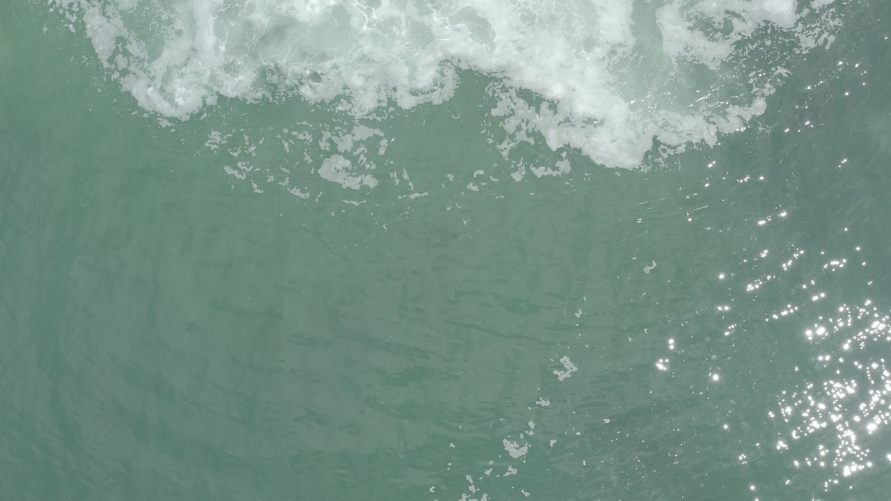 Foamy surf over green water with sunlight glittering at the right.