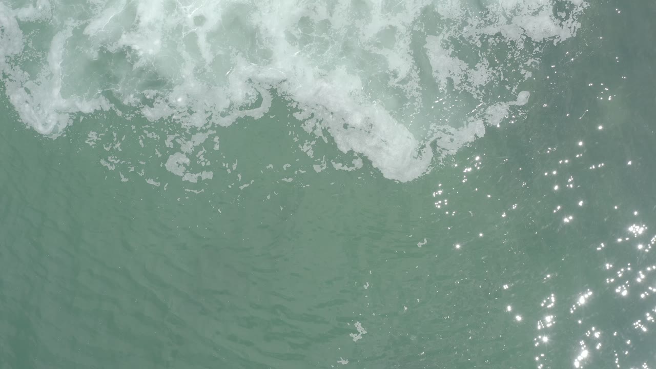 Overhead green ocean water with foam at the top and sparkles to the right.