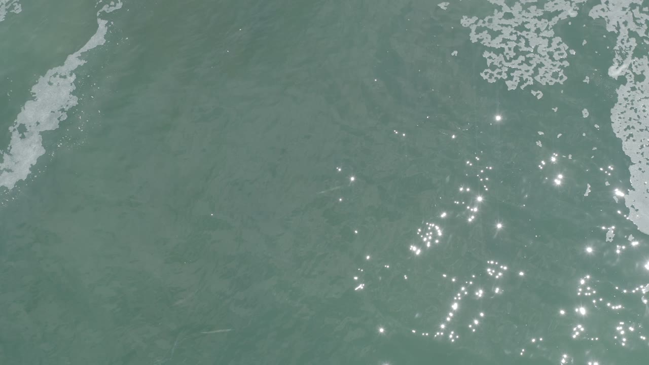 Open ocean with foam at the top and sun sparkles to the right