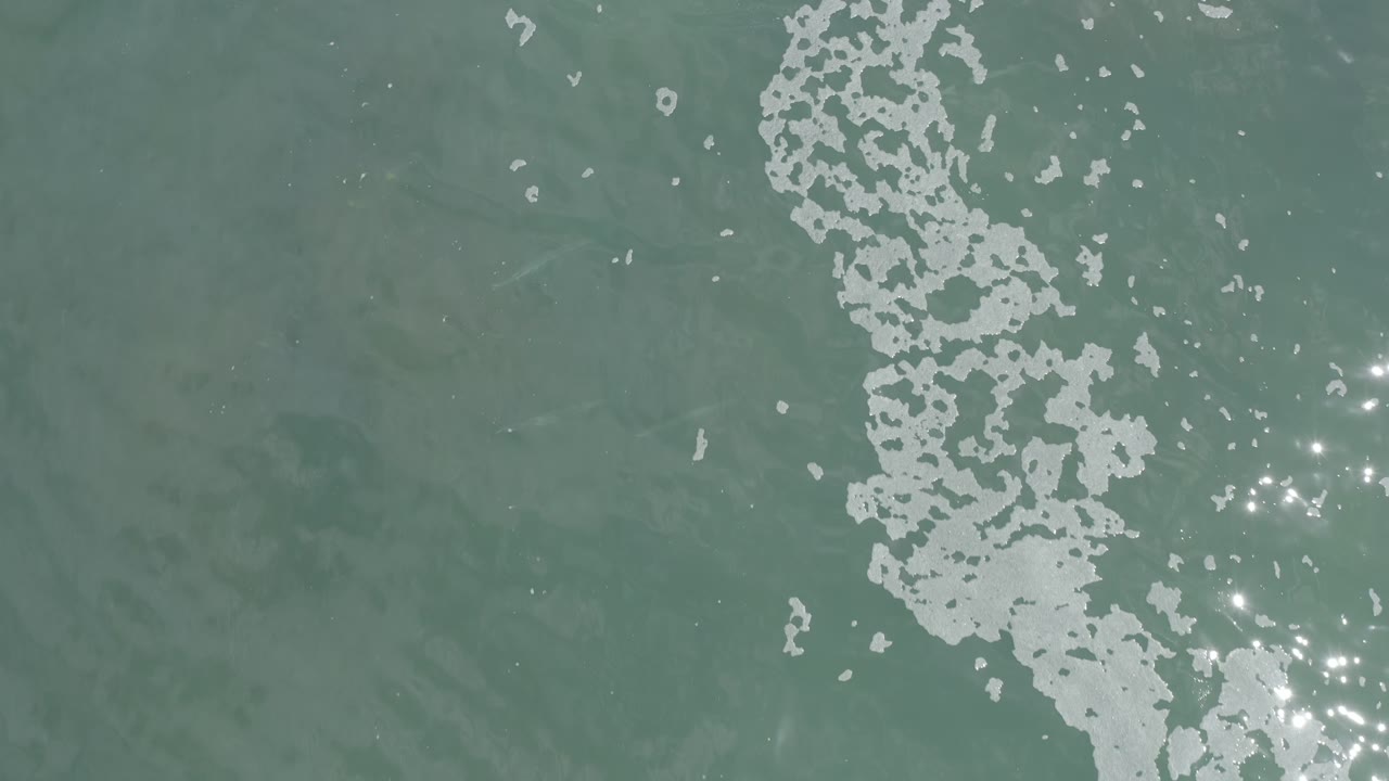 Overhead Los Cabos water surface with scattered white foam crossing the center and bright sparkle points clustered toward the lower right, with no visible people.