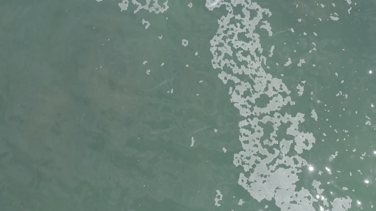 Foam and sun sparkle over blue-green water