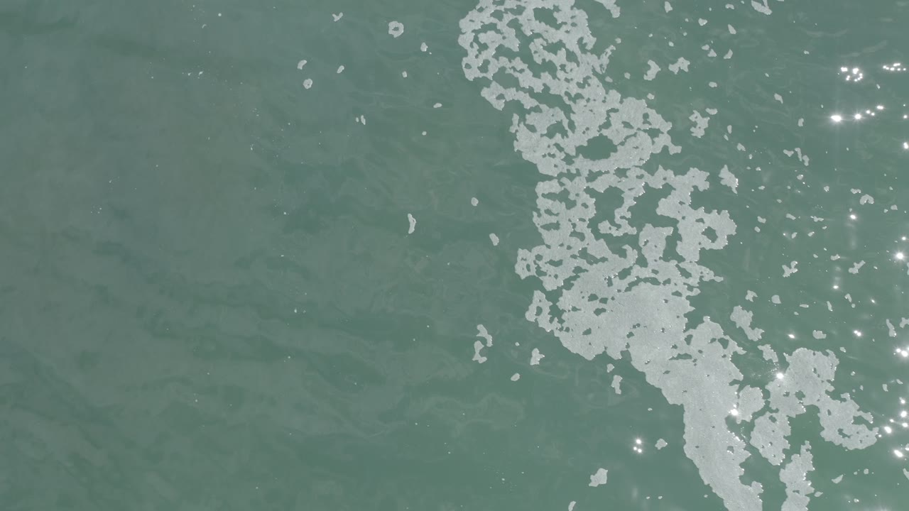 Green ocean water with foam near the upper right and scattered light reflections.