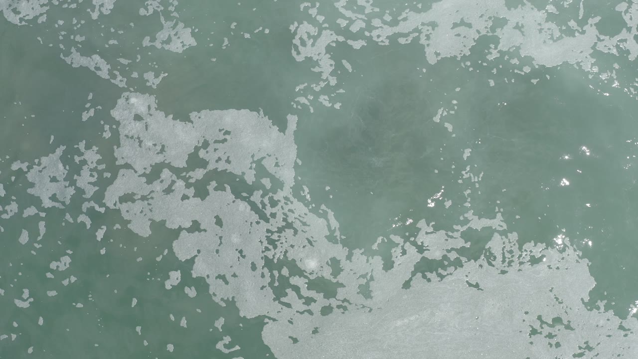 Top-down turquoise ocean water with white foam patches