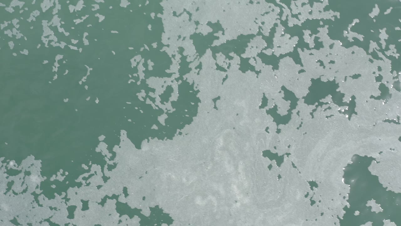 Dense white sea foam over muted green water.