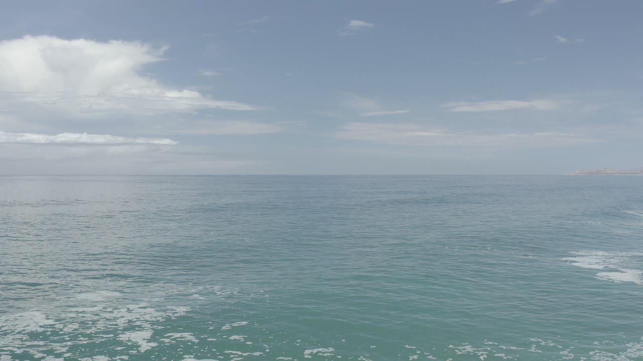 Blue ocean under a pale cloudy sky with foam near the bottom of frame.