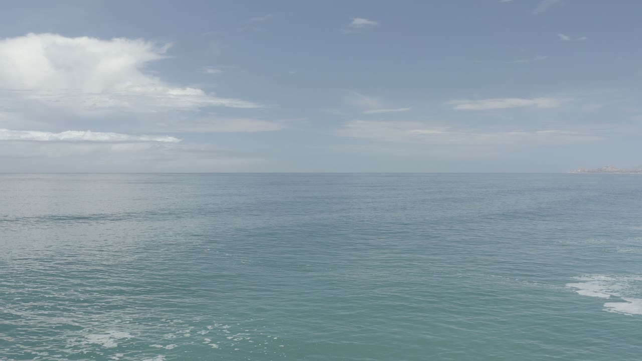 Los Cabos sea surface at one second, showing a broad empty horizon, muted clouds, faint land on the right edge, and no visible people.