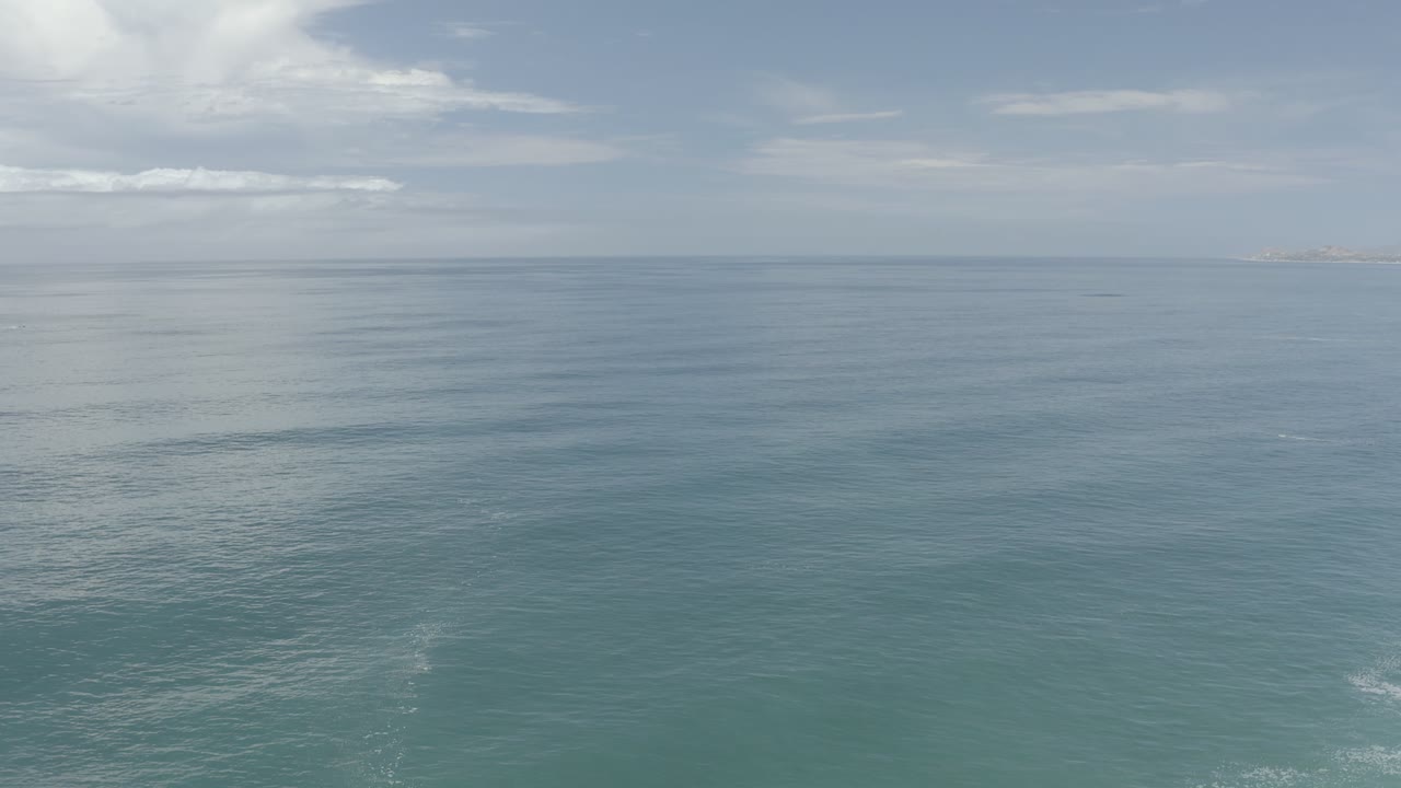 Second frame shows the Los Cabos ocean surface with subtle ripple texture, thin clouds across the sky, faint land near the right horizon, and no visible people.
