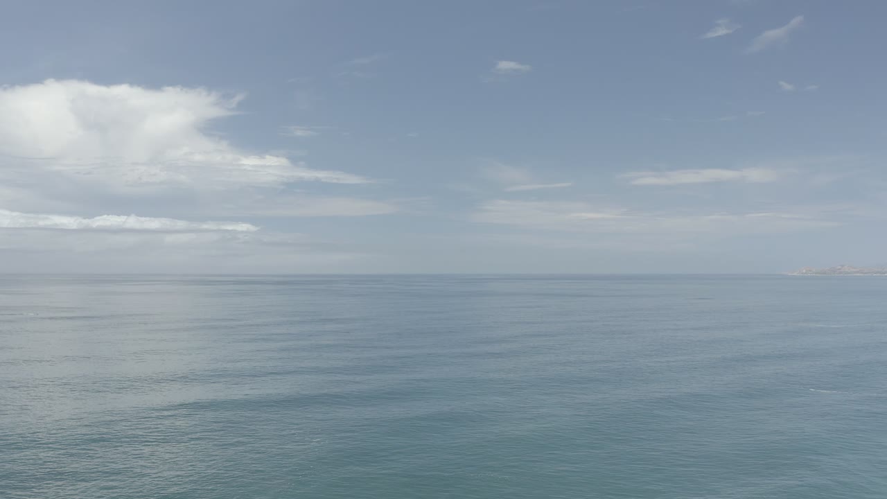 The Los Cabos ocean remains broad and still, with a compact white cloud cluster above the horizon and no visible people or vessels.
