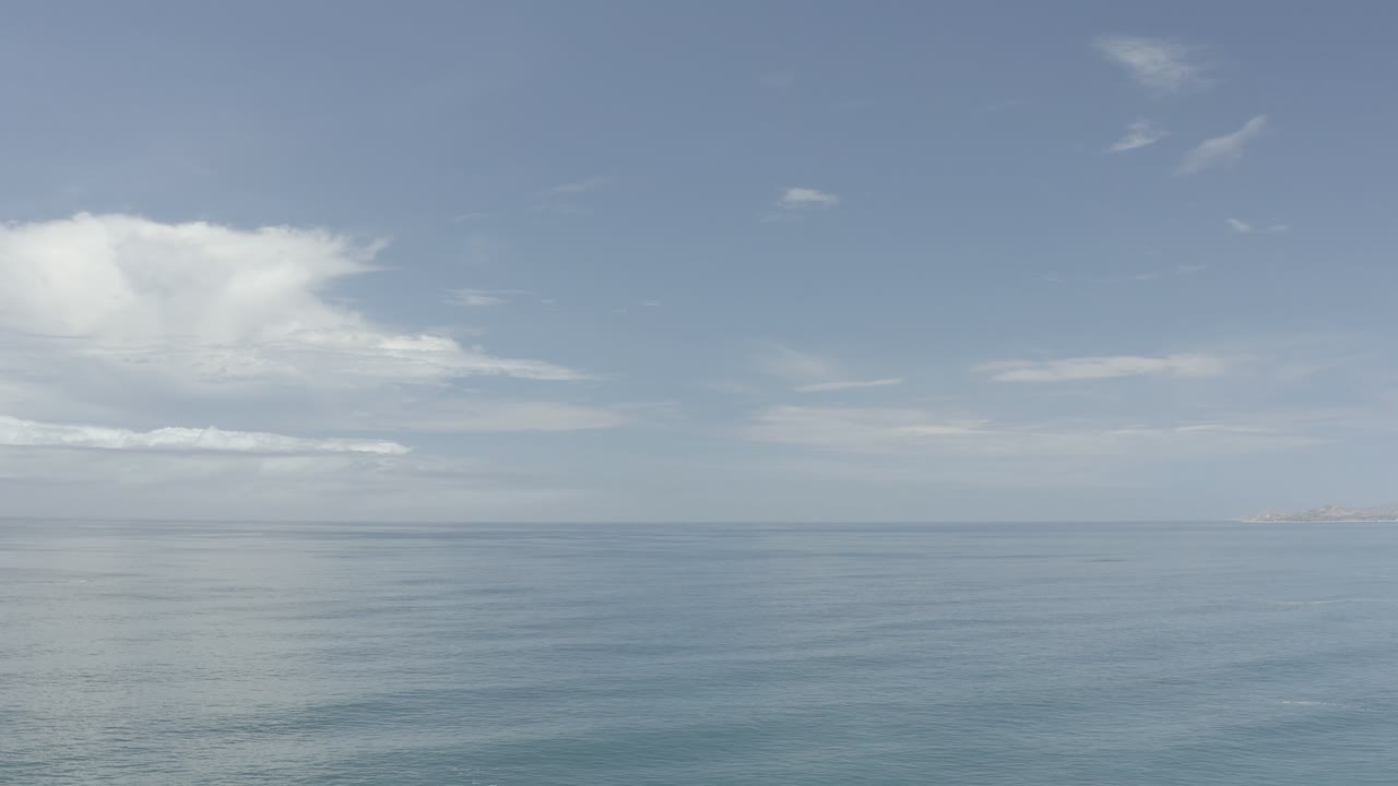 Los Cabos ocean view with small ripples across the water, pale clouds overhead, and no visible people.