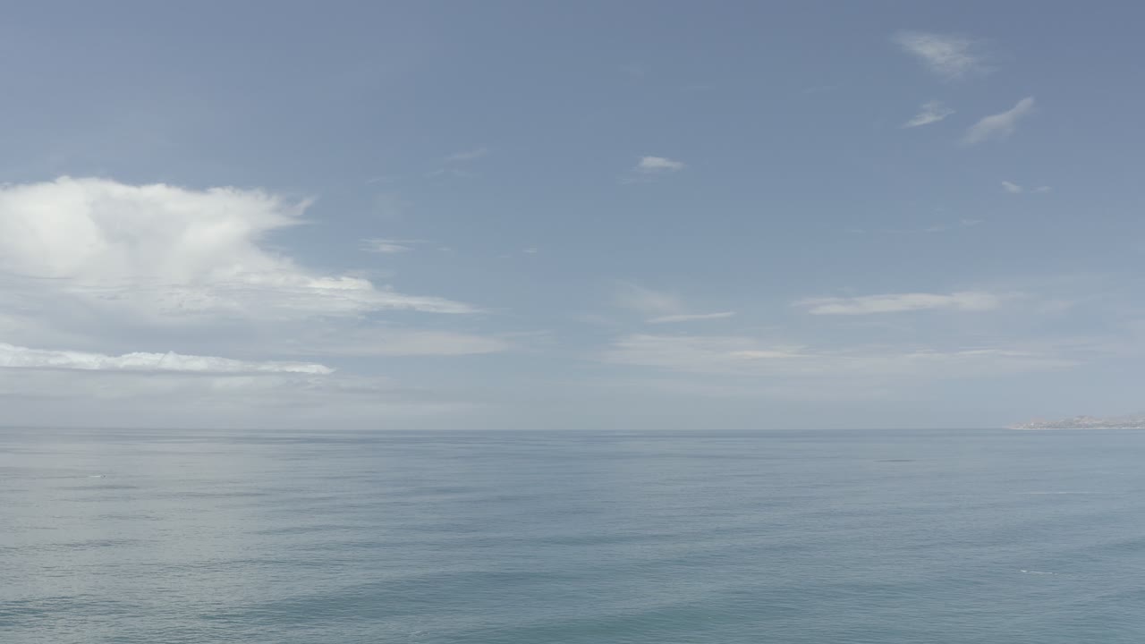 Opening frame of calm Los Cabos ocean water beneath a pale sky, with white clouds on the left and no visible people.