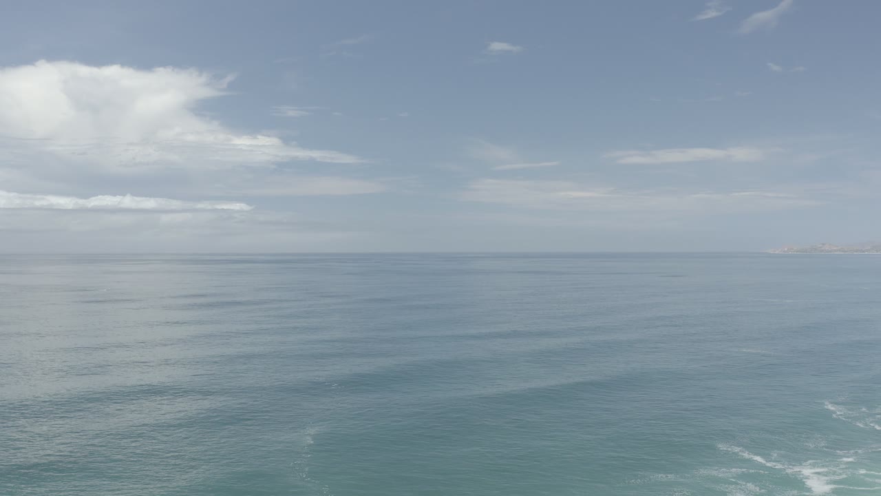 Wide ocean horizon with clouds and faint surf below.
