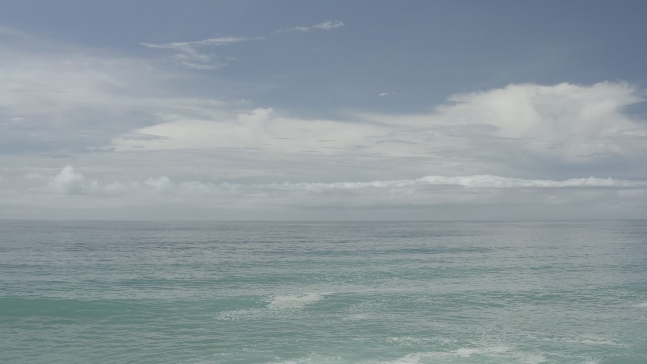 Opening frame of the Los Cabos, Mexico coastline with blue-green water, white surf near the bottom edge, layered clouds, and no visible people.