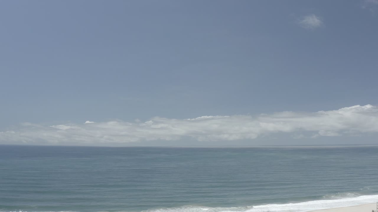 Wide ocean horizon under pale blue sky with surf at the bottom edge.