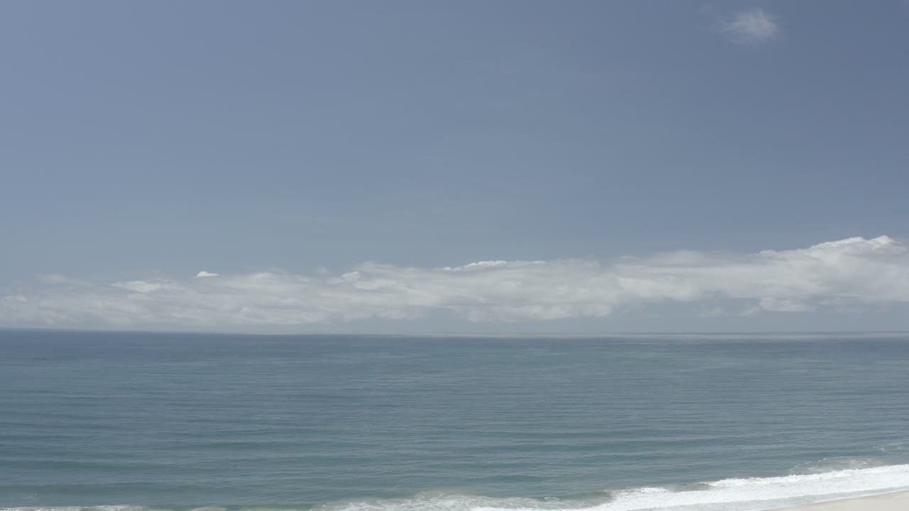 Open ocean beneath a blue sky, with a foamy wave along the lower right.