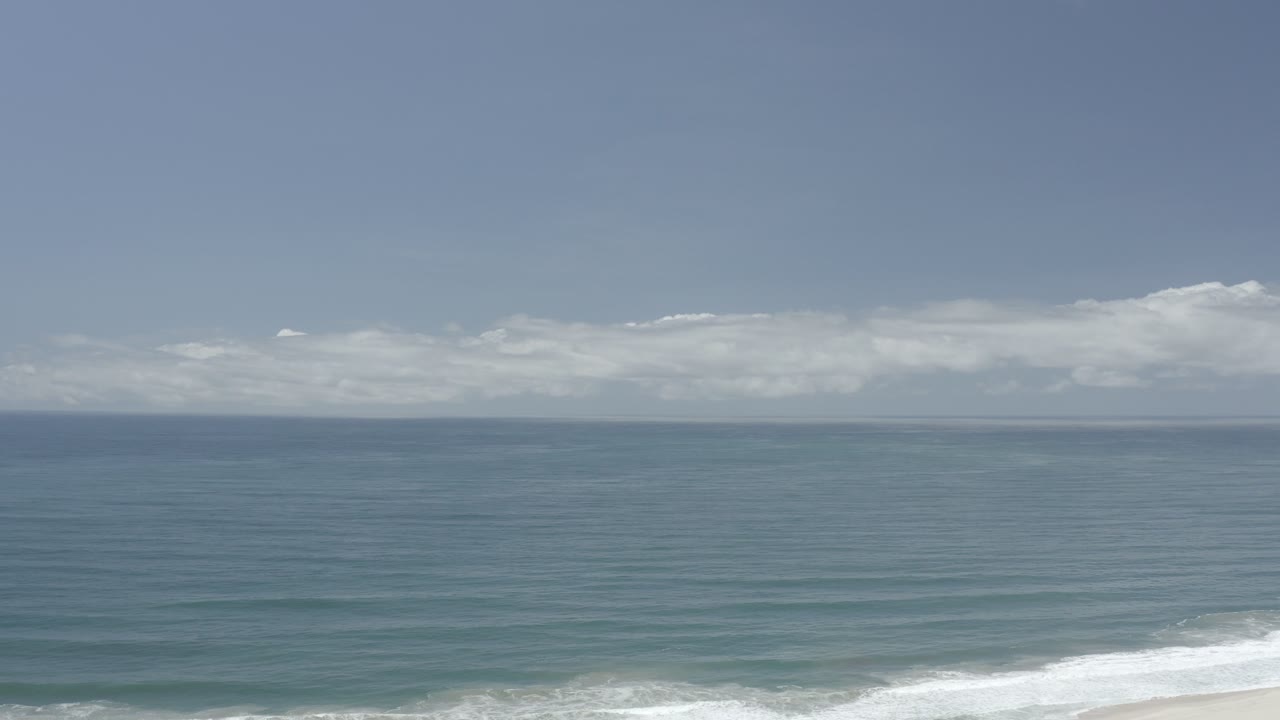 Opening frame of a Los Cabos, Mexico beach view with blue-green water, a level horizon, low white clouds, white surf at the lower edge, and no visible people.