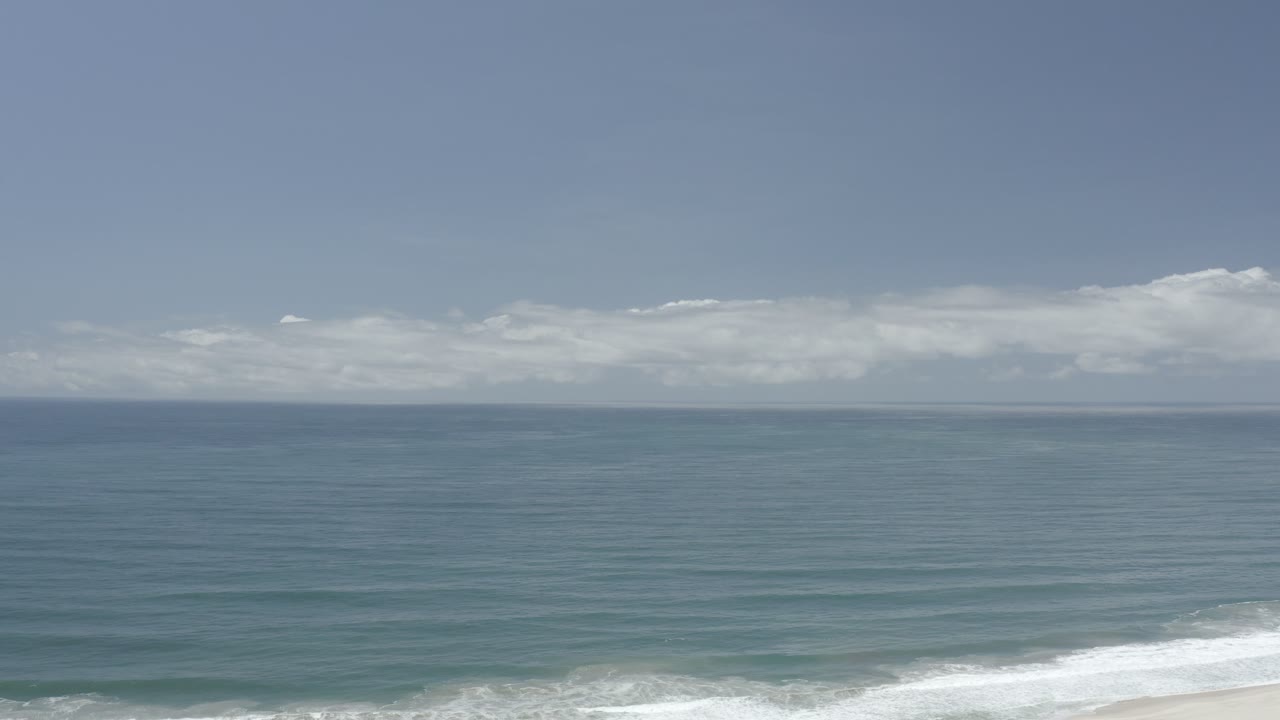 Calm blue-green water, distant cloud bank, and foamy shoreline surf