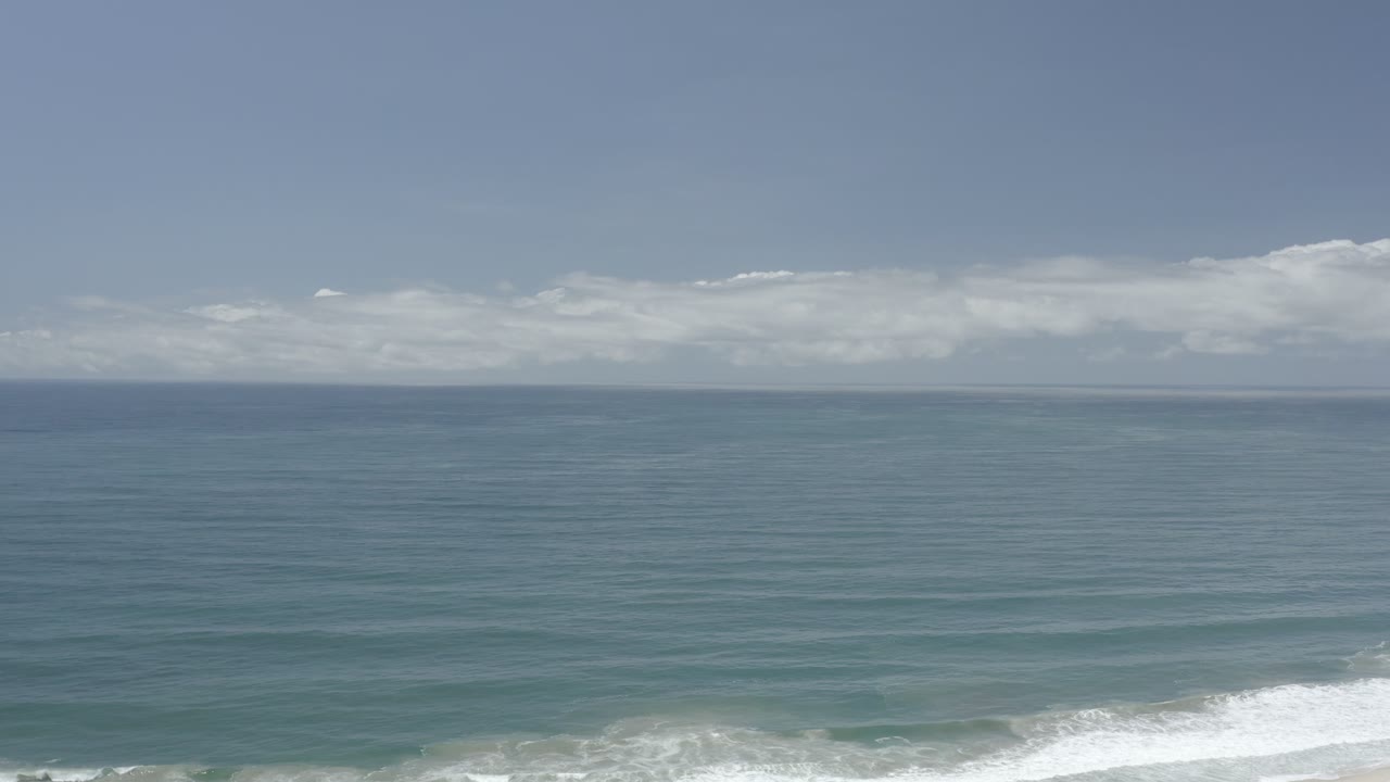 The second frame holds on a broad Los Cabos sea surface with a straight horizon, layered cloud band, and white breaking water along the bottom edge, with no visible people.