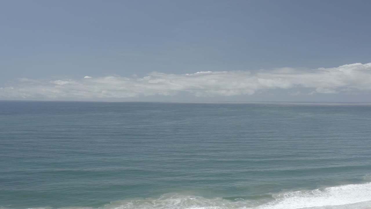 Open ocean with distant clouds and shorebreak below