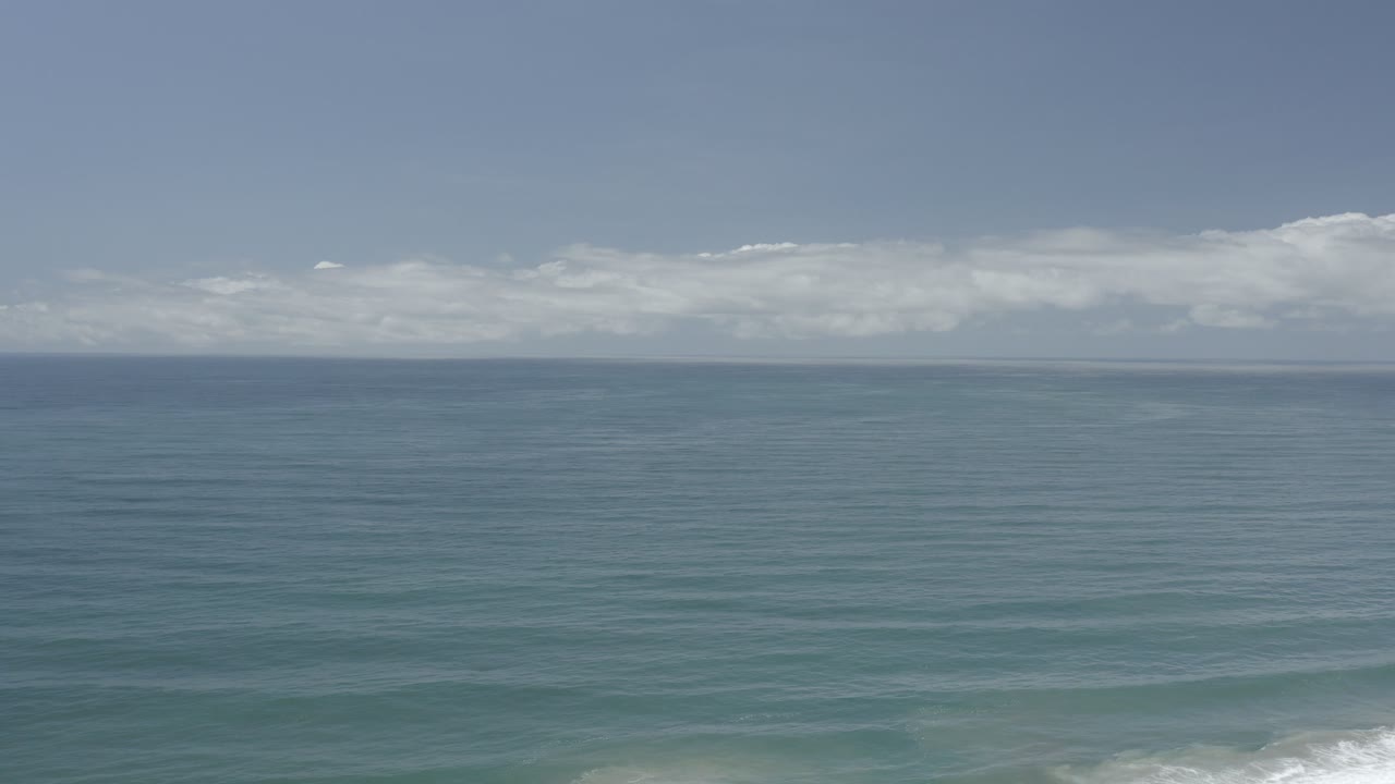 Blue ocean below a pale sky and low white clouds.