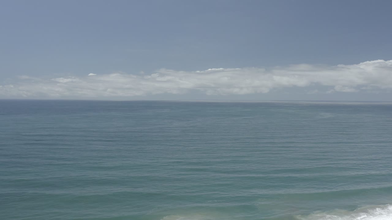 Los Cabos, Mexico ocean view with the horizon held near midframe, soft white clouds stretching across the distance, and no visible people.