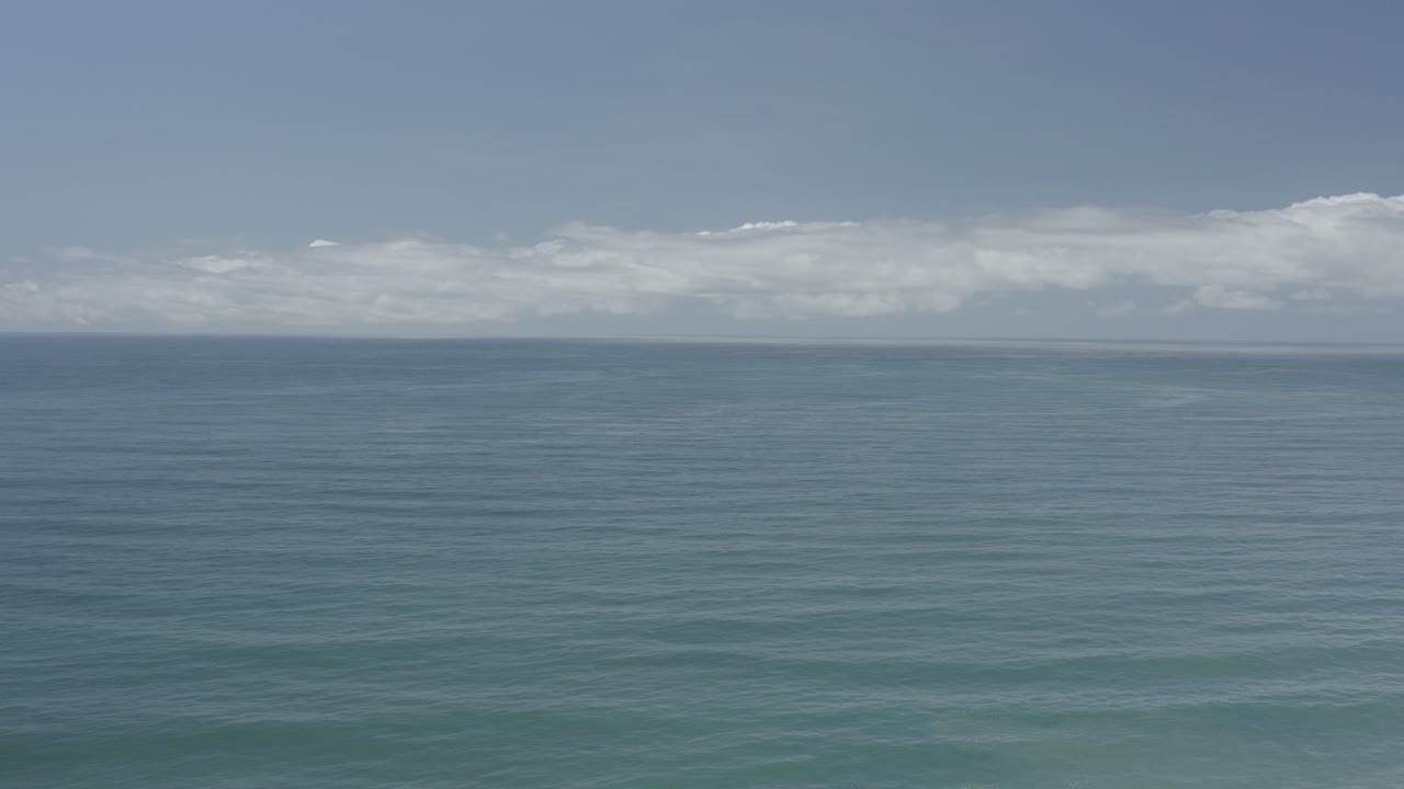Opening frame of blue ocean in Los Cabos, Mexico, with faint parallel wave rows, a high horizon, low white clouds, and no visible people.