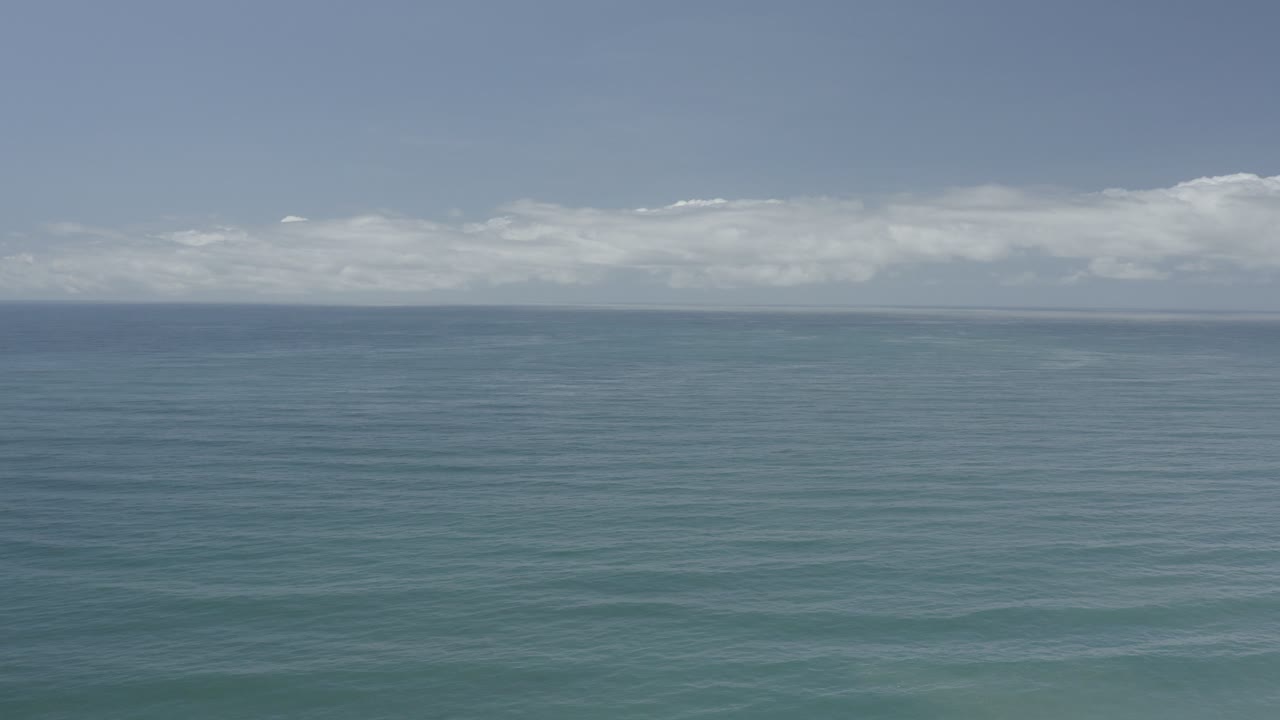 Open ocean under bright sky with white cloud bands near the horizon.