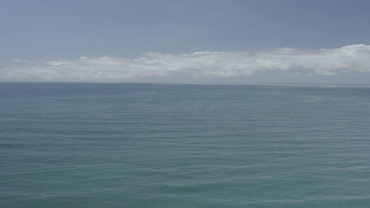 Opening frame of blue-green ocean off Los Cabos with a level horizon, pale sky, low white clouds, and no visible people.