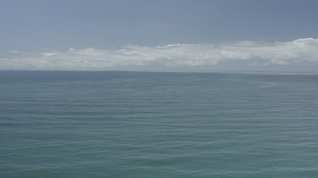 Blue-green water stretches to a distant horizon in Los Cabos, with a broad band of low clouds and no visible people.